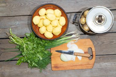 Eski ahşap bir masada patates pişirmek. Tahta bir masada, sarı bir tencerede çiğ patates. Eski tahta tahtalar ve sebzeler.