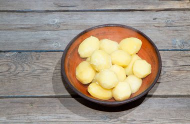 Eski ahşap bir masada patates pişirmek. Tahta bir masada, sarı bir tencerede çiğ patates. Eski tahta tahtalar ve sebzeler.