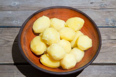 Eski ahşap bir masada patates pişirmek. Tahta bir masada, sarı bir tencerede çiğ patates. Eski tahta tahtalar ve sebzeler.