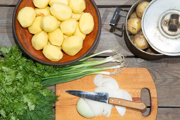 Eski ahşap bir masada patates pişirmek. Tahta bir masada, sarı bir tencerede çiğ patates. Eski tahta tahtalar ve sebzeler.