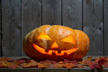 Düşen yaprakların ortasında, ahşap bir masanın üzerinde balkabağı feneri. Cadılar Bayramı tatili. Ahşap bir duvarın arkasında balkabağı ve düşen yapraklar..