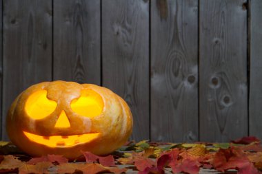 Düşen yaprakların ortasında, ahşap bir masanın üzerinde balkabağı feneri. Cadılar Bayramı tatili. Ahşap bir duvarın arkasında balkabağı ve düşen yapraklar..