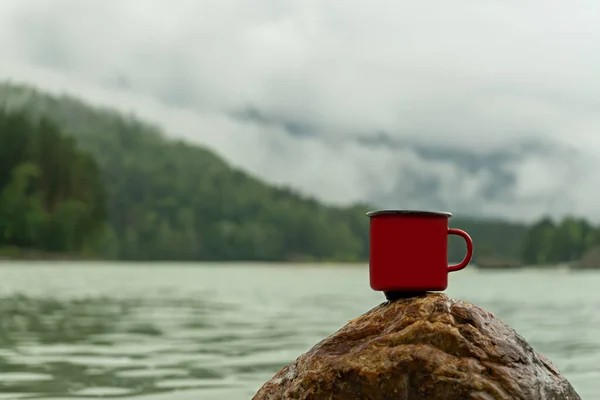 Red enamel mug on a mountain rock, beautiful mountain view, blurred background