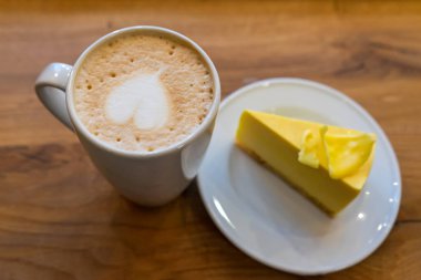 Kahverengi ahşap masada kekli cappuccino bardağı