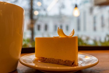 Tabaktaki cheesecake, pencerenin önündeki kahverengi masada, bardakta içkinin yanında.