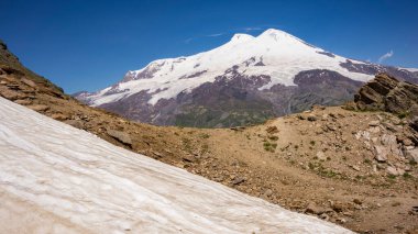 Volkan Elbrus, Rusya 'nın Kabardino-Balkaria bölgesindeki Kafkasya dağlarının güneydoğusunda hareketsiz bir volkandır. Cheget Mount yamacından görüntü. Ön planda kar var. İrtifa 3050 metre..