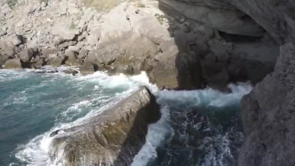 Salpicaduras de agua. El agua del mar late contra las rocas. Las olas del mar de agua oscura golpean contra las rocas costeras. Un número infinito de salpicaduras, gotas de agua y espuma blanca se dispersan. — Vídeo de stock