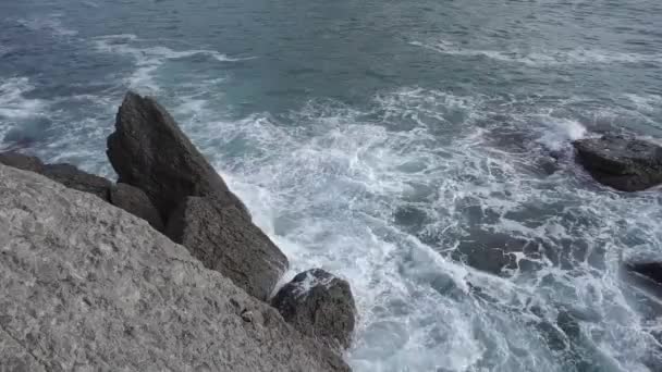 Salpicaduras de agua. El agua del mar late contra las rocas. Las olas del mar de agua azul-gris golpean contra las rocas costeras. Un número infinito de salpicaduras, gotas de agua y espuma blanca se dispersan. Novy Svet — Vídeos de Stock