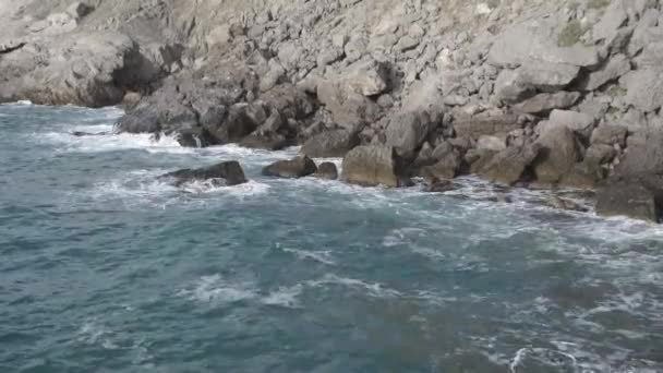 Salpicaduras de agua. El agua late contra la orilla del mar. Las olas del mar de agua azul golpean las rocas costeras. Un número infinito de salpicaduras, gotas de agua de mar y espuma blanca se dispersan. Novy Svet — Vídeos de Stock