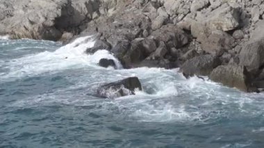 Su sıçrıyor. Deniz kıyısına karşı su çarpar. Deniz dalgaları kıyı kayalarına vuruyor. Mavi-gri su dalgaları kıyı kayalarına vuruyor. Novy Svet. Kırım.