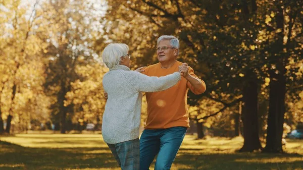Parkta dans eden mutlu yaşlı çift. Kıdemli adam yaşlı bir kadınla flört ediyor. Yaşlılıkta romantizm sonbahar günü — Stok fotoğraf