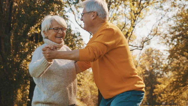 Счастливая старая пара танцует в парке. Старший мужчина флиртует с пожилой женщиной. Романтика в старости осенний день — стоковое фото