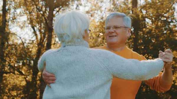 Pareja feliz bailando en el parque. Hombre mayor coqueteando con una anciana. Romance a la vejez el día de otoño —  Fotos de Stock