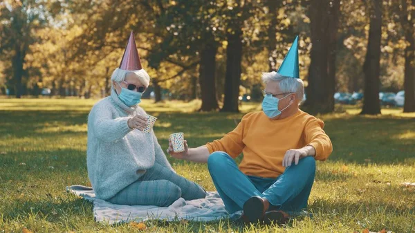 Celebração de aniversário no parque durante o covid-19. Casal de idosos com mascaramento facial jogo de cartas — Fotografia de Stock