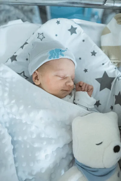 Liebenswertes Neugeborenes schläft friedlich in seinem Kinderbett im Krankenhauszimmer mit Stofftier — Stockfoto