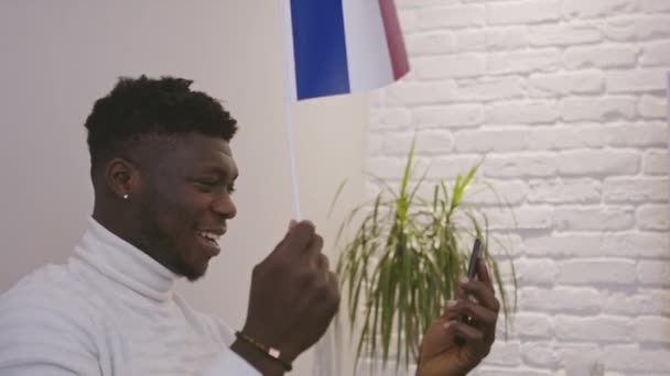 Чёрный мужчина, который звонил на смартфон, размахивая флагом Франции — стоковое видео