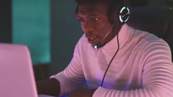 Távoli munka. Fekete férfi, munkamániás, laptoppal megvilágított fejhallgatóval — Stock videók