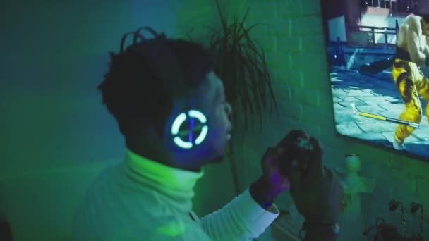 Чёрный человек играет в видеоигры с помощью джойстик-контроллера. Радость и домашнее развлечение ночью — стоковое видео