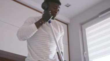 Genç ve mutlu yakışıklı zenci adam floranı temizlerken müziği dinliyor ve dans ediyor.