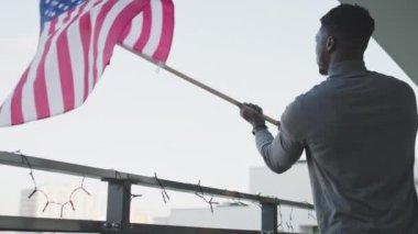 Genç çekici siyah adam balkondan Amerikan bayrağı sallıyor.