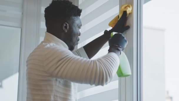 アフリカ系黒人の男がアパートを衛生してる。窓枠を拭く — ストック動画