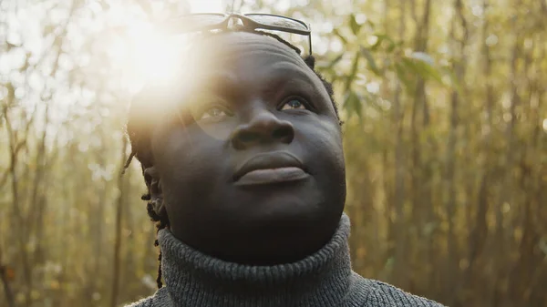 Portrét mladého Afričana v lese, jak vzhlíží k obloze. Sluneční paprsky procházející stromy — Stock fotografie