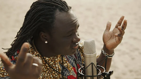 Close up de um homem africano de camisa tradicional cantando em um microfone condensador no deserto — Fotografia de Stock