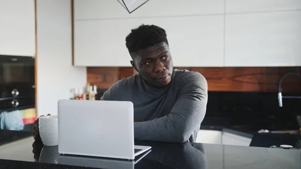 Jovem negro afro-americano trabalhando em laptop em seu apartamento esticando e olhando pela janela — Fotografia de Stock