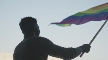 LGBT hakları ve onur etkinlikleri için protestocuların arasında gökkuşağı bayrağı sallayan siyah adam