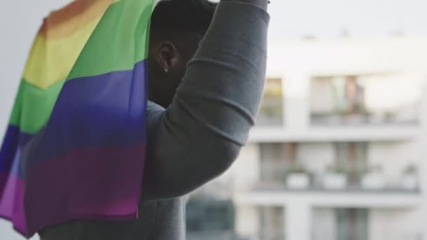 Uomo nero che tiene bandiera arcobaleno e sventola dietro la schiena dal balcone — Video Stock