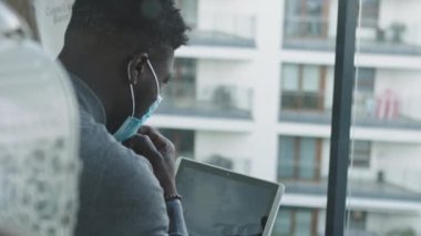 Dizüstü bilgisayarda çalışan Afro-Amerikan siyah adam. Çay ya da kahve içmek için yüz maskesi çıkarıyorum. Yeni önleyici tedbirlerle ofis çalışması