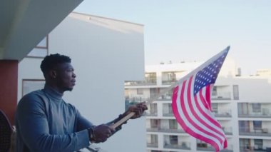 Siyah adam balkondan Amerikan bayrağı sallıyor.