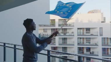 Genç siyahi sığınmacı, balkondan Avrupa Birliği bayrağı sallıyor.
