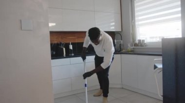Mutfakta yerleri temizlerken dans edip şarkı söyleyen mutlu siyah adam. yerel yaşam konsepti