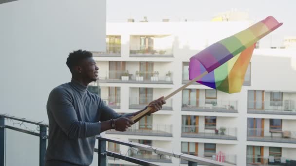 Ung svart man aktivist viftande regnbåge flagga från balkongen — Stockvideo