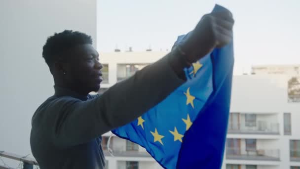 Mladý černoch žadatel o azyl mává evropskou unijní vlajkou z balkónu