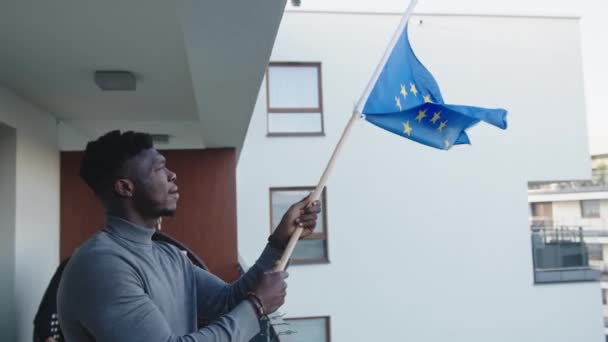 Młody czarny człowiek azyl osoba machając european flaga związek z balkonu — Wideo stockowe