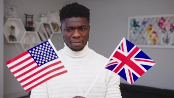 Verwarde zwarte man die VS en Britse vlaggen vasthoudt. Immigratiekeuze — Stockvideo