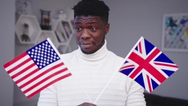 Homem negro confuso segurando bandeiras dos EUA e do Reino Unido. Escolha da imigração — Vídeo de Stock