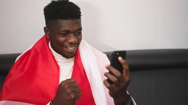 Polonyalı bayraklı genç, mutlu siyah adam akıllı telefondan maç izliyor. — Stok fotoğraf
