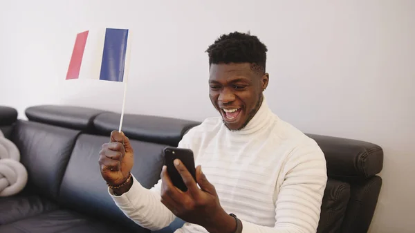Genç siyahi adam akıllı telefondan maç seyrediyor ve Fransa bayrağı sallıyor. — Stok fotoğraf
