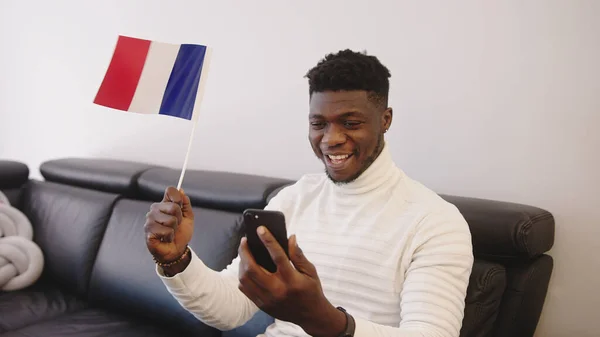 Joven hombre negro viendo el juego en el teléfono inteligente y ondeando la bandera de Francia —  Fotos de Stock