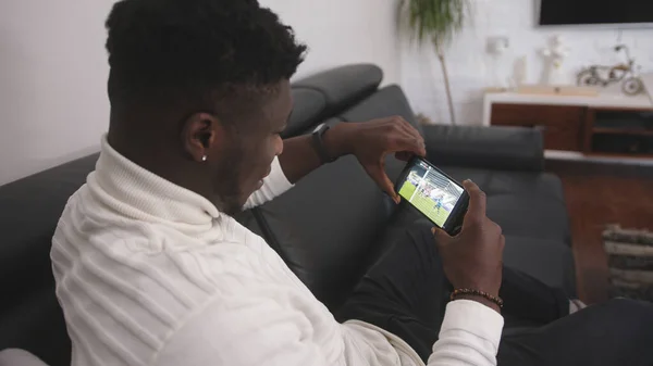 Joven hombre negro emocionado viendo el partido de fútbol en el teléfono inteligente — Foto de Stock