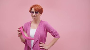 Kırmızı kısa saçlı olgun bir kadın, yüksek iyileştirici ayakkabılar giyiyor. Mor arka planda izole edilmiş.