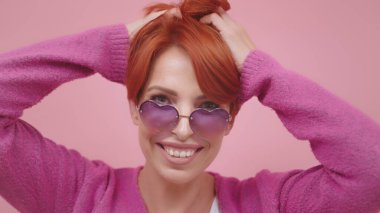 Kalp şeklinde gözlüklü, kızıl saçlarını elleriyle tutan orta yaşlı güzel bir kadının portresi. Güzel atış.