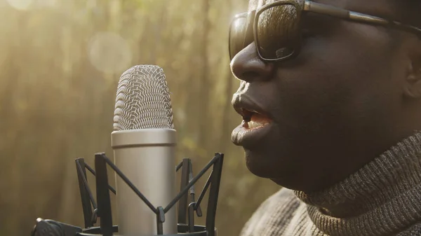 Portret van Afro-Amerikaanse zwarte man die zingt in de microfoon in het bos. Natuurlijk licht — Stockfoto