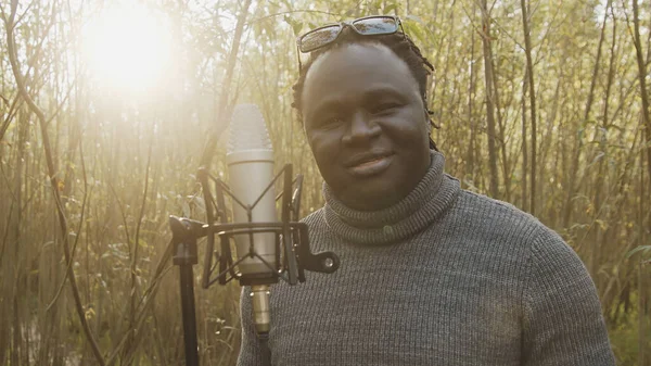 Jonge Afro-Amerikaanse zwarte man die zingt in de microfoon in het bos. Natuurlijk licht — Stockfoto