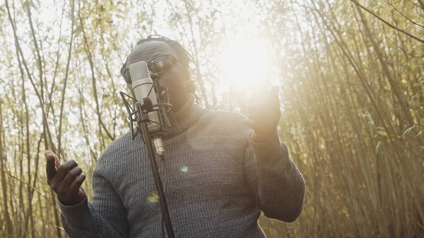 Mladý affrican muž zpívající v přírodě, sluneční paprsky procházející mezi stromy — Stock fotografie