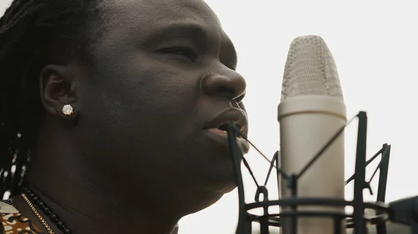 Mladý Afričan v tradičním barevném oblečení zpívá v mikrofonu. Zavřít — Stock fotografie