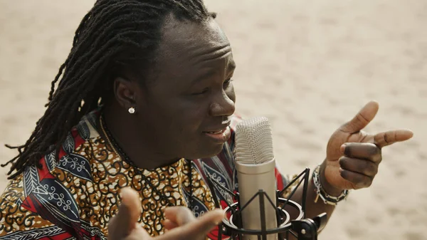 Geleneksel tişörtlü Afrikalı bir adamın çölde daha yoğun bir mikrofona şarkı söylemesi. — Stok fotoğraf